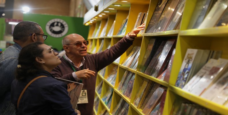 Personas mirando libros en una estantería en la Filbo