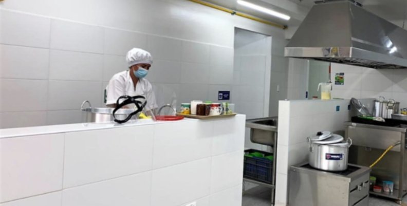 Comedor comunitario Mujer vestida con traje de cocinera al lado de una estufa de un comedor comunitario