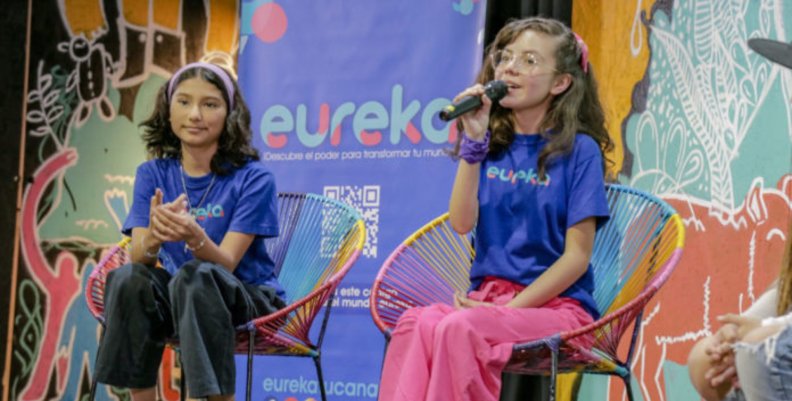 Niños de la Generación Eureka Dos niñas sentadas en una tarima
