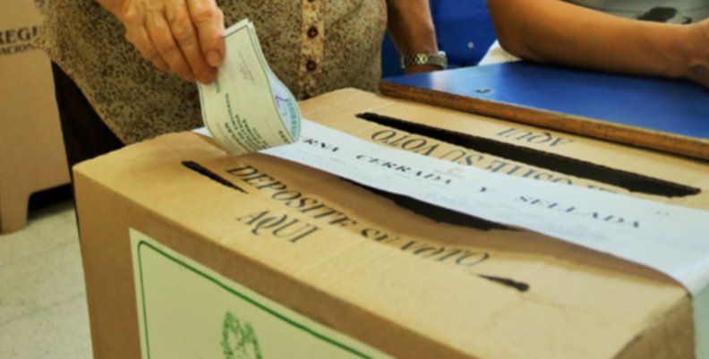 Elecciones Caja de cartón. Una mano introduce un papel verde en ella