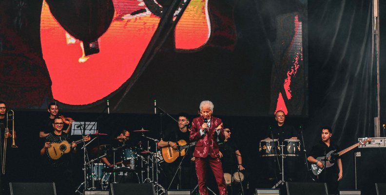 Galy Galiano Hombre con traje morado con brillantes, en medio de una tarima con músicos
