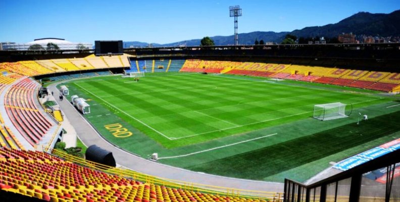 El Campín Vista panorámica de un estadio con gradas rojas y amarillas y césped verde en el medio