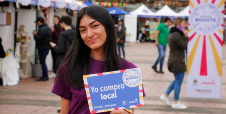 Mujer con camiseta morada sosteniendo un cartel de Hecho en Bogotá