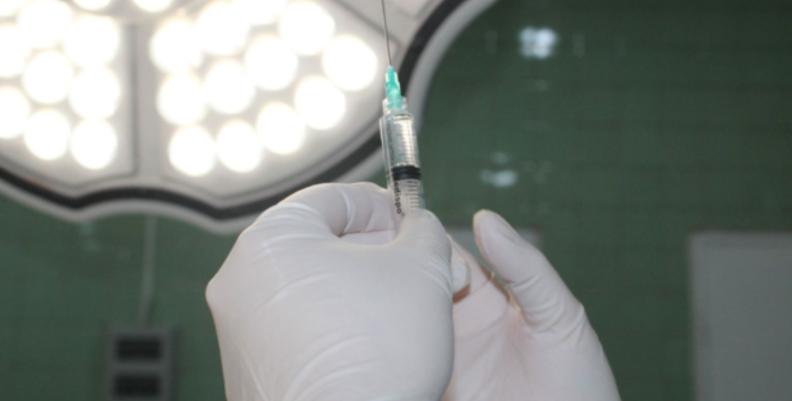 Manos con guantes quirúrgicos que sostiene una aguja hipodérmica