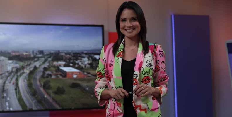 Mujer sonriente con blazer color rosa sobre un fondo morado