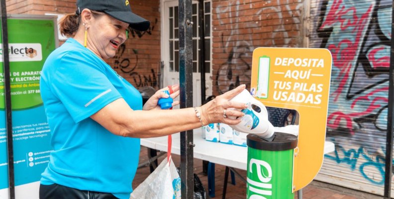 Reciclaje en Engativá Mujer con camiseta azul depositando una botella en un cesto verde