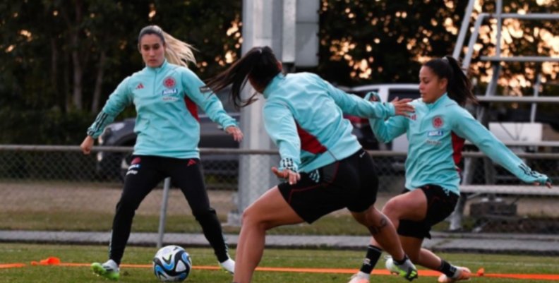 Fútbol Tres mujeres con uniforme color celeste disputando un balón blanco, paradas en pasto color verde