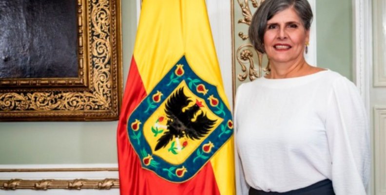 Veedora Distrital La veedora distrital está al lado de una bandera amarilla y roja con el escudo de Bogotá
