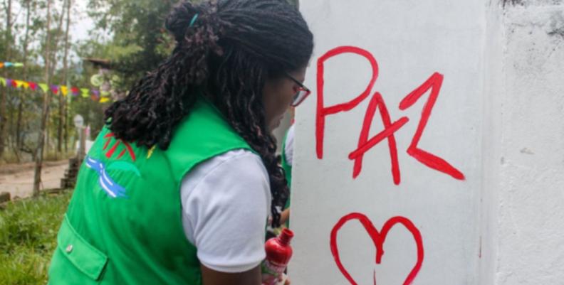 Mujer haciendo un grafiti que dice "Paz" en una pared blanca
