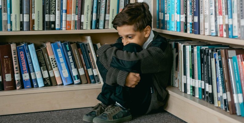 Especial de datos web AHORA: matoneo en los colegios públicos Niño triste en un rincón de un escaparate con libros