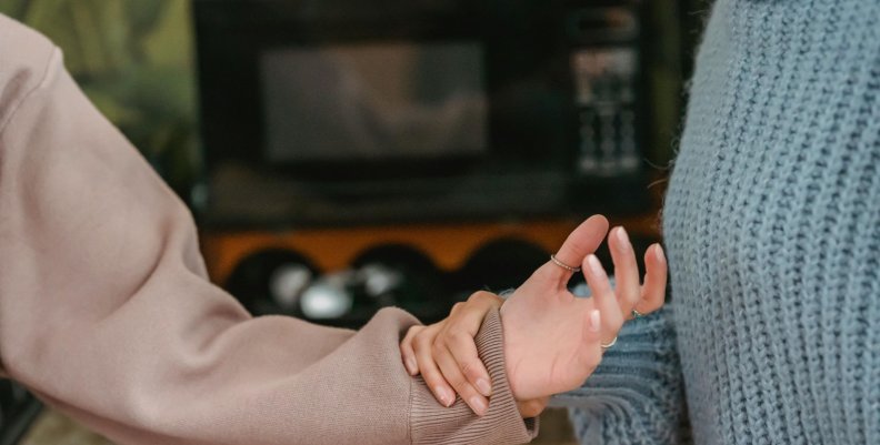 Maltrato Una persona con saco gris le sostiene la mano a otra con saco café.
