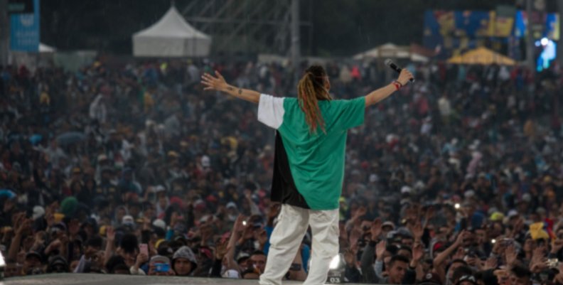 Foto de Hip Hop al Parque 2022. Hombre en el escenario con camisa verde y pantalón blanco abre los brazos frente al público