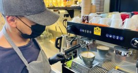 Hombre con mandil y tapabocas preparando café