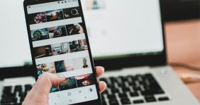 Un celular con imágenes de plantas y al fondo un computador encendido