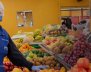 Mujer con indumentaria para manipulación de alimentos al lado de una plaza de mercado con frutas y verduras