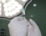 Manos con guantes quirúrgicos que sostiene una aguja hipodérmica