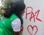 Mujer haciendo un grafiti que dice "Paz" en una pared blanca