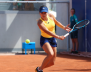 Mujer con ropa deportiva: shorts azules, blusa amarilla y jugando tenis 