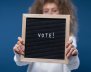 Niño sostiene un tablero con la palabra Voto