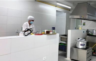 Mujer vestida con traje de cocinera al lado de una estufa de un comedor comunitario
