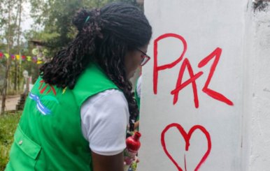 Mujer pintando una pared con la palabra "Paz"