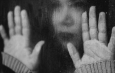 Mujer con las manos frente a una ventana empapada en blanco y negro