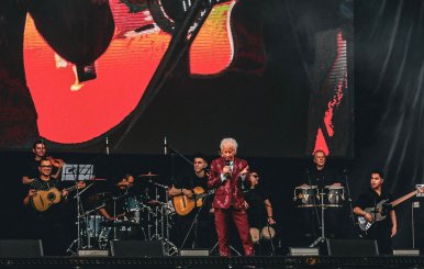 Hombre con traje morado con brillantes, en medio de una tarima con músicos