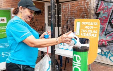 Mujer con camiseta azul depositando una botella en un cesto verde 