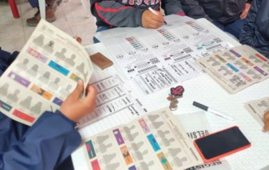 Manos encima de una mesa en la que aparecen papeles de votación para una elección local.