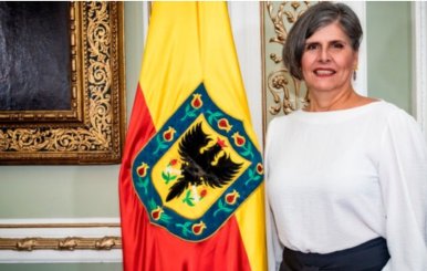 La veedora distrital está al lado de una bandera amarilla y roja con el escudo de Bogotá