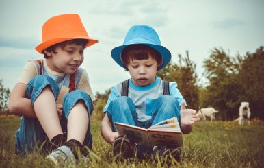 Dos niños en el césped leyendo un libro