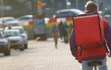 Domiciliario transitando en bicicleta por la ciudad con una mochila cuadrada de color naranja