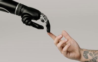 Una mano humana tocando con el dedo índice a una mano robótica.