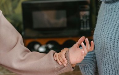 Una persona con saco gris le sostiene la mano a otra con saco café. 